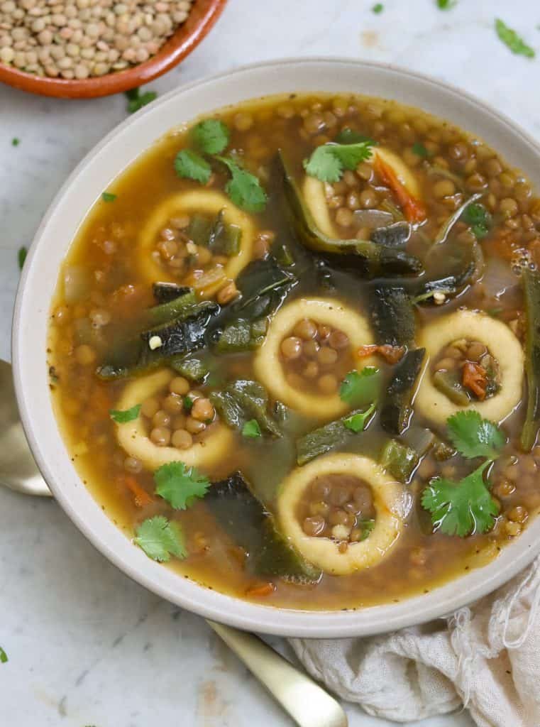 chochoyotes with lentil soup in a bowl on a white surface.