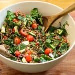 lentil kale salad in a mixing bowl on a wooden cutting board.