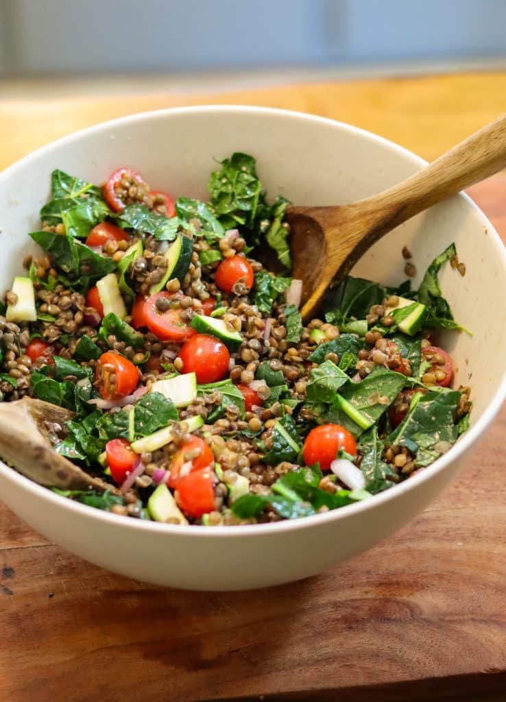 lentil kale salad in a mixing bowl on a wooden cutting board.