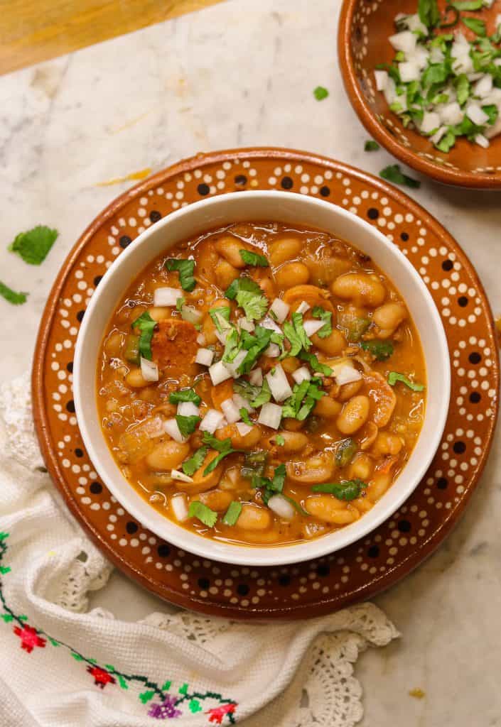charro beans in a white bowl with cilantro and onions on top.
