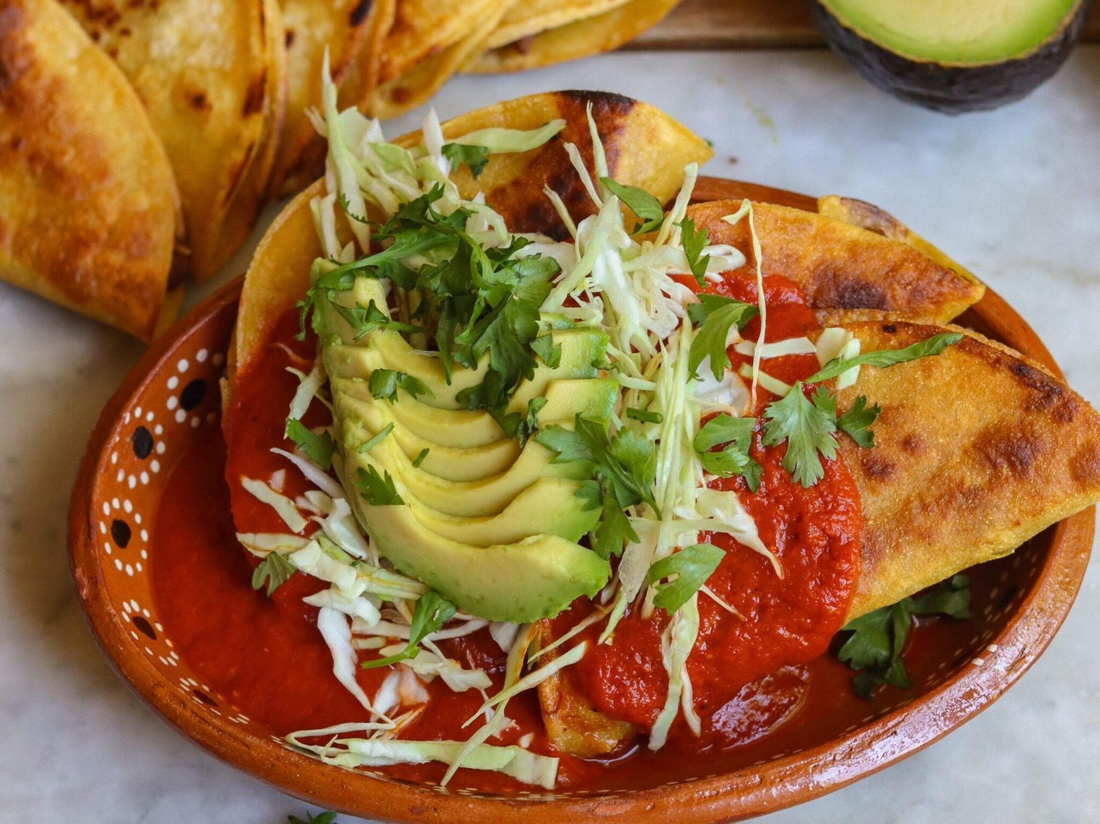 drowned tacos in a mexican dish with toppings and avocado.